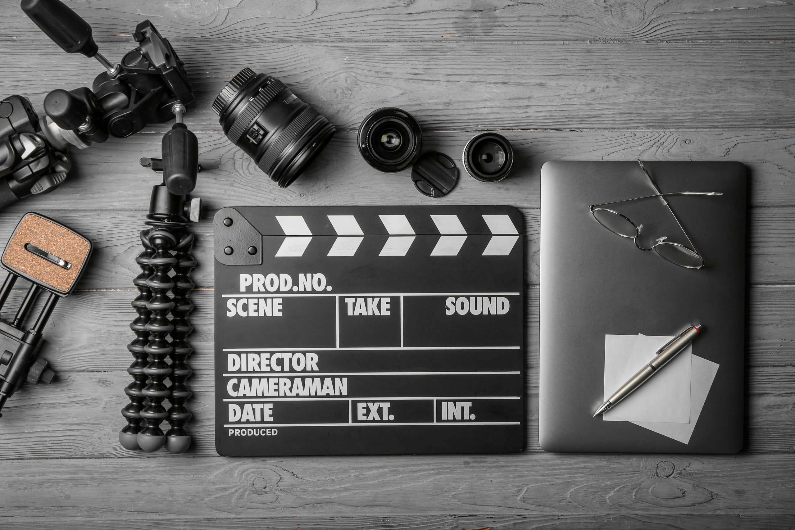 Composition with movie clapper, laptop and different lenses on grey background, top view